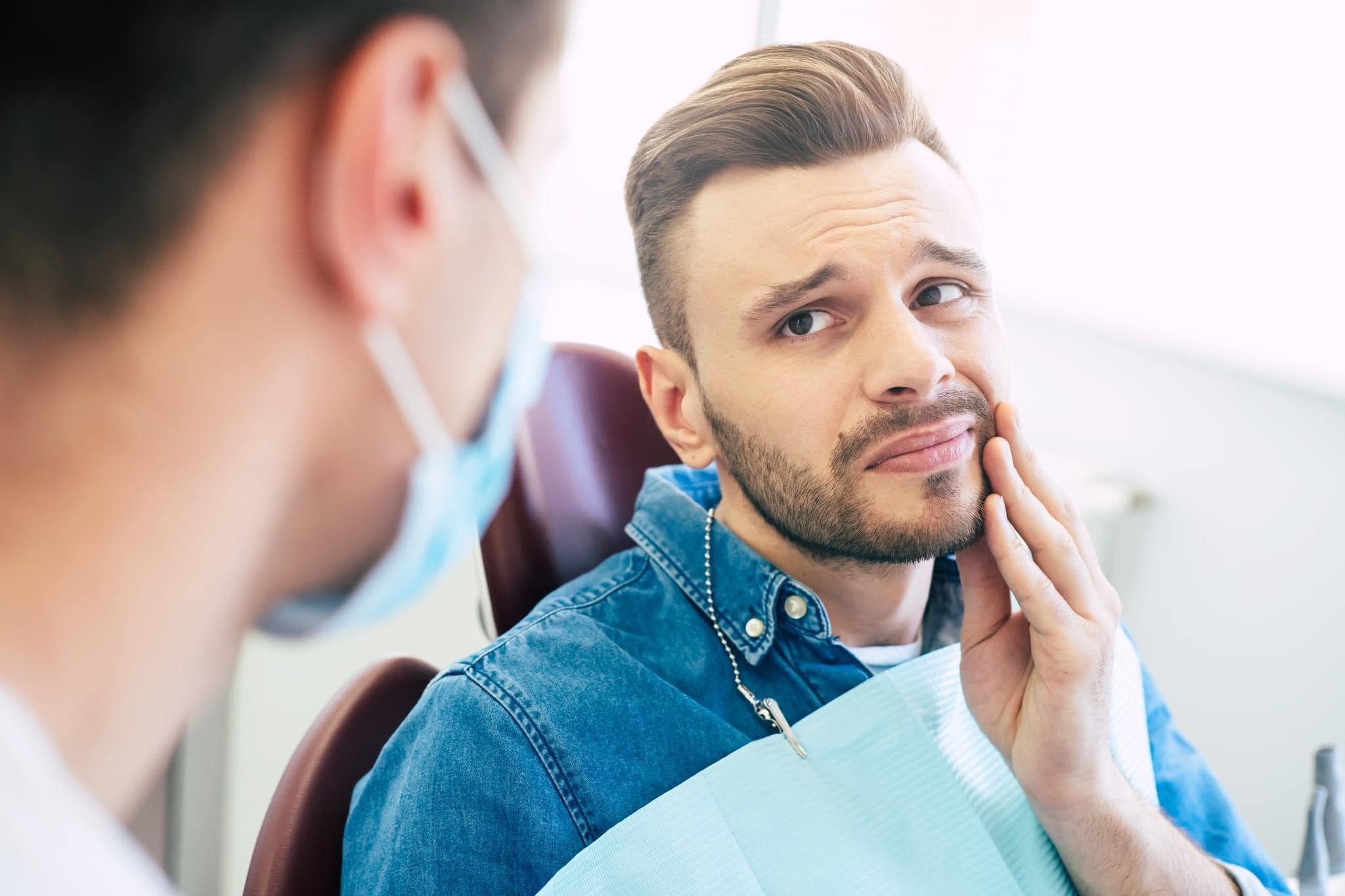 Image of a distressed patient with a dental emergency, holding their jaw with a concerned expression. The patient appears to be in discomfort, possibly due to toothache or injury. They are sitting in a dental chair, awaiting prompt dental care and relief.